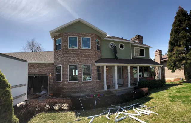 Two-story house with brick facade, green siding, porch, and chimney on a sunny day.
