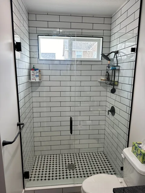 Glass shower enclosure with white subway tile and black hardware