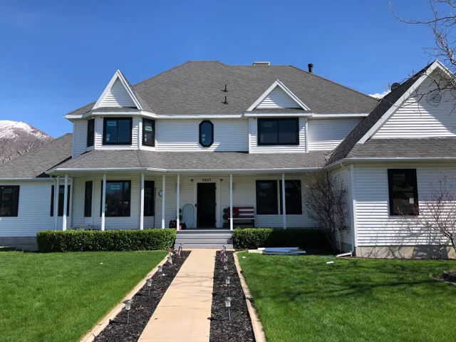 White house with dark trim, gray roof, front porch, pathway to door. Green grass, blue sky.