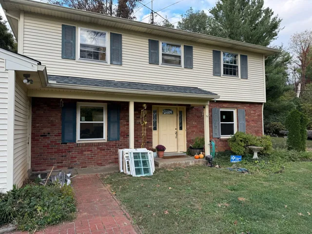 Two-story house with brick and beige siding, blue shutters, and a yellow door on a grassy lawn.