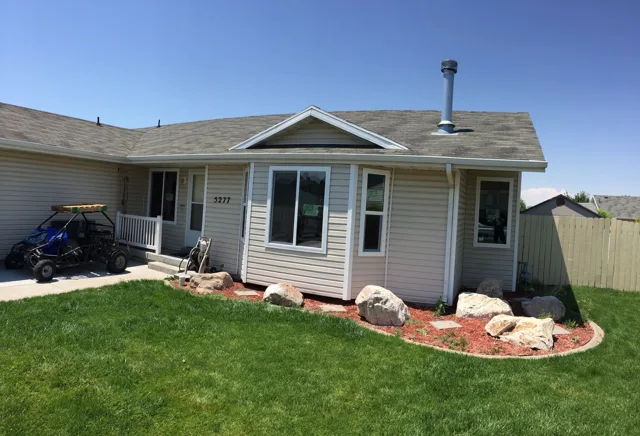 Beige house with green lawn and decorative rocks, blue sky in the background.