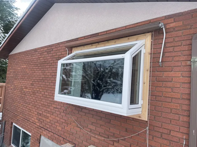 A bay window on a brick house, installed in a wooden frame. Winter setting.